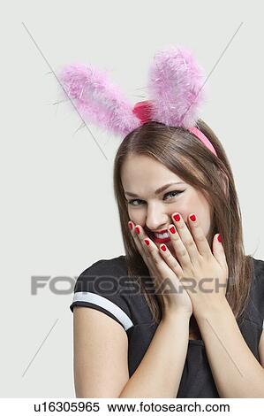 Shy young woman wearing rabbit ears over gray background View Large Photo Image Stock Photography - Shy young woman wearing rabbit ears over gray background. Fotosearch