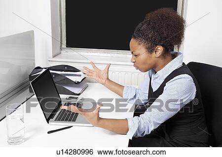 Stock Photograph - Side view of frustrated young businesswoman looking at laptop in office. Fotosearch