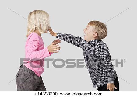 Stock Image - Side view of playful young boy and girl over white background. Fotosearch
