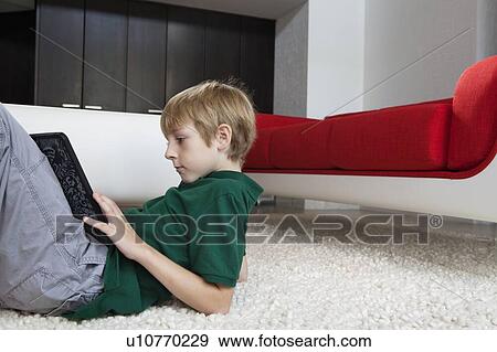 Stock Photo - Side view of young boy using tablet pc while lying on rug. Fotosearch