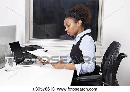 Side view of young businesswoman with document using laptop at desk in office View Large Photo Image Stock Image - Side view of young businesswoman with document using laptop at desk in office. Fotosearch