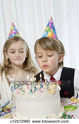 Stock Image - Sister watching while birthday boy blowing candles on cake. Fotosearch