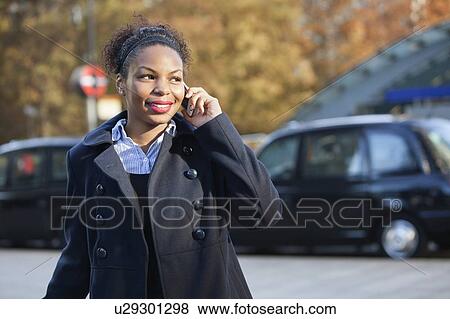 Stock Photo - Smiling African American young woman using mobile phone outdoors. Fotosearch