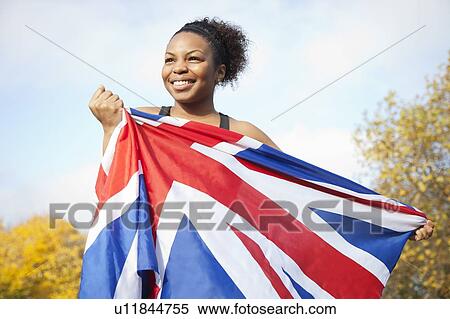 Smiling young woman holding British flag against trees and sky View Large Photo Image Stock Photography - Smiling young woman holding British flag against trees and sky. Fotosearch