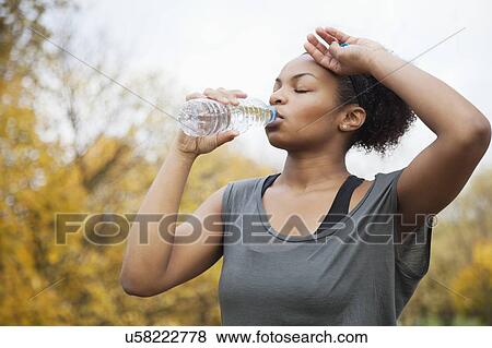 Stock Photo - Sporty young woman drinking water in park. Fotosearch