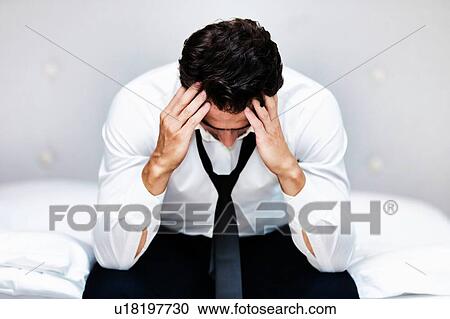 Stock Image - Stressed and overworked businessman sitting on the bed. Fotosearch