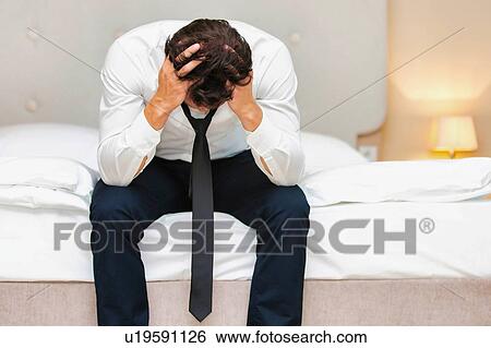 Stressed and overworked businessman sitting on the bed View Large Photo Image Stock Photograph - Stressed and overworked businessman sitting on the bed. Fotosearch