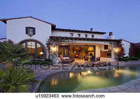 Stock Image - Swimming pool in front of luxury manor house under evening lights. Fotosearch