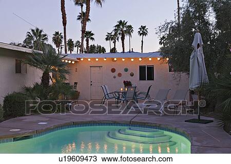 Stock Image - Swimming pool with chaise lounge in evening lights. Fotosearch