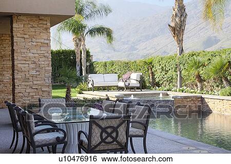 Stock Photograph - Table and chair at poolside patio in manor house. Fotosearch