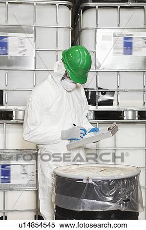 Stock Photography - Technician in hazmat suit taking down notes of chemical in drum. Fotosearch