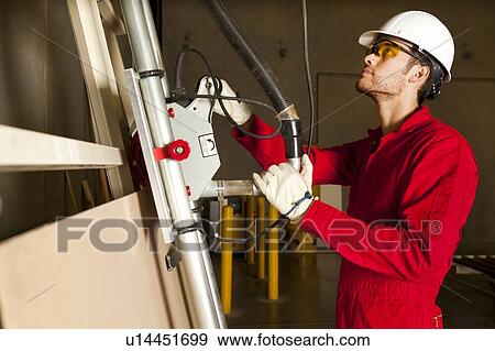 Stock Photo - Technician operating heavy duty machinery in manufacturing plant. Fotosearch