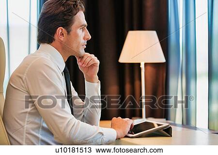 Thoughtful businessman using digital tablet while sitting with lens flare View Large Photo Image Stock Image - Thoughtful businessman using digital tablet while sitting with lens flare. Fotosearch