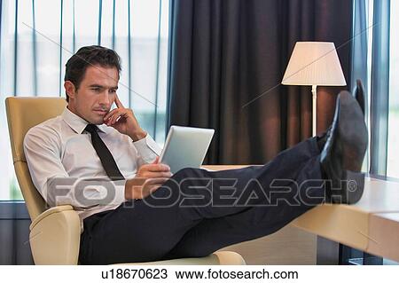 Stock Image - Thoughtful businessman using digital tablet while sitting with lens flare. Fotosearch
