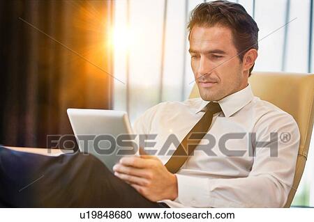 Thoughtful businessman using digital tablet while sitting with lens flare View Large Photo Image Stock Image - Thoughtful businessman using digital tablet while sitting with lens flare. Fotosearch