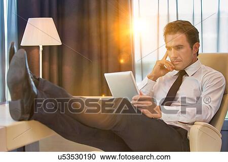 Thoughtful businessman using digital tablet while sitting with lens flare View Large Photo Image Stock Image - Thoughtful businessman using digital tablet while sitting with lens flare. Fotosearch