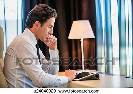 Thoughtful businessman using digital tablet while sitting with lens flare View Large Photo Image Stock Photo - Thoughtful businessman using digital tablet while sitting with lens flare. Fotosearch