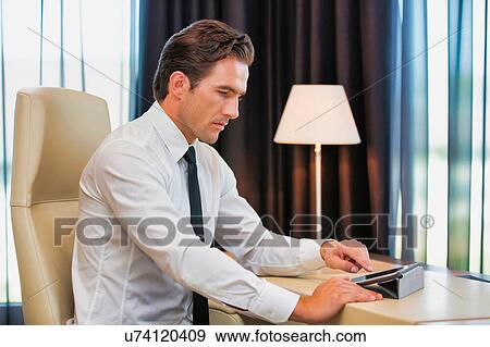 Stock Photo - Thoughtful businessman using digital tablet while sitting with lens flare. Fotosearch