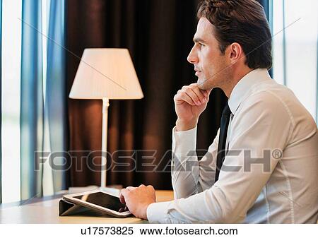 Thoughtful businessman using digital tablet while sitting with lens flare View Large Photo Image Stock Photography - Thoughtful businessman using digital tablet while sitting with lens flare. Fotosearch
