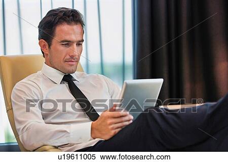 Stock Photography - Thoughtful businessman using digital tablet while sitting with lens flare. Fotosearch