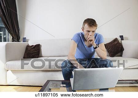 Stock Photography - Thoughtful man using laptop while sitting on sofa at home. Fotosearch