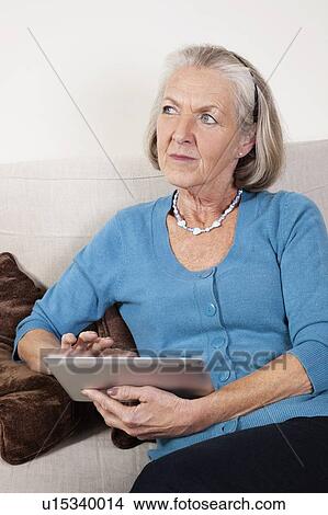 Picture - Thoughtful senior woman using digital tablet at home. Fotosearch