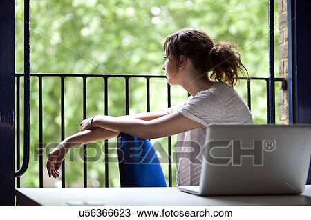 Stock Image - Thoughtful young businesswoman sitting at desk by balcony. Fotosearch
