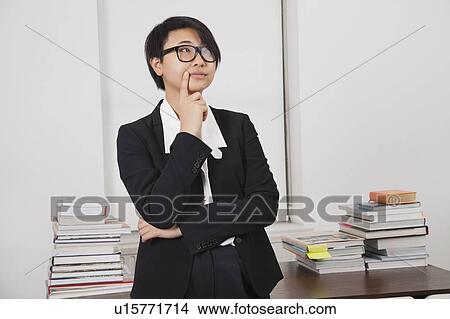 Thoughtful young businesswoman with stack of books on desk in office View Large Photo Image Picture - Thoughtful young businesswoman with stack of books on desk in office. Fotosearch