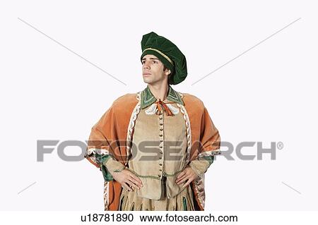 Stock Image - Thoughtful young man in old-fashioned costume with hands on hips against gray background. Fotosearch