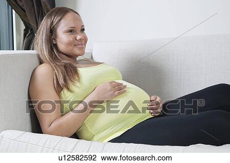 Stock Image - Thoughtful young pregnant woman relaxing on sofa at home. Fotosearch