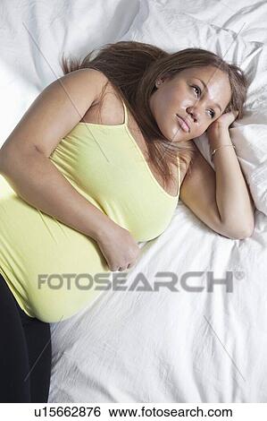 Stock Photograph - Thoughtful young pregnant woman relaxing on bed at home. Fotosearch