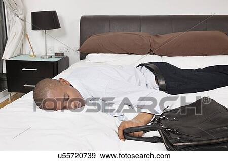 Stock Photo - Tired young African American businessman sleeping in bed. Fotosearch