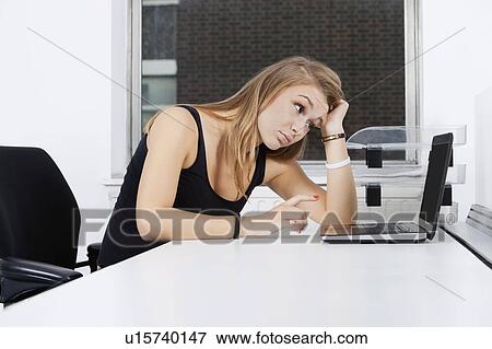 Tired young businesswoman looking at laptop in office View Large Photo Image Stock Photo - Tired young businesswoman looking at laptop in office. Fotosearch