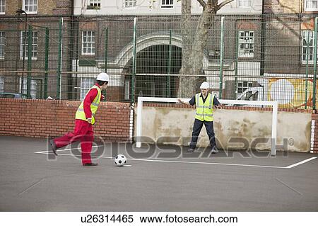 Stock Photography - Two manual workers playing football. Fotosearch