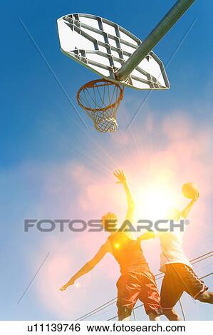 Stock Photograph - Two men playing basket ball in strong sunshine. Fotosearch
