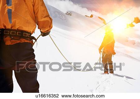 Stock Image - Two mountaineers hiking in mountains holding ropes. Fotosearch
