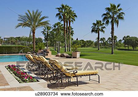 Picture - View of sun loungers at poolside with lawn in background. Fotosearch