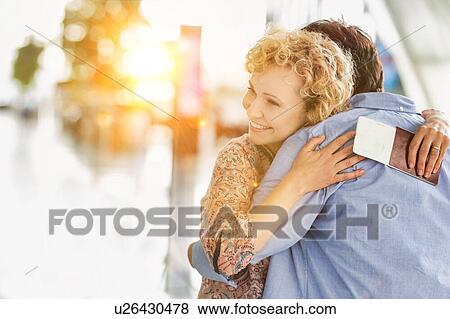 Stock Photo - Wife reuniting with his husband in airport with yellow lens flare. Fotosearch