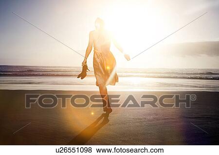 Woman walking on beach wearing dress and holding high heels View Large Photo Image Stock Photo - Woman walking on beach wearing dress and holding high heels. Fotosearch