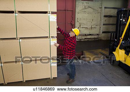 Stock Photo - Worker inspecting wood pallet standing by fork lift truck. Fotosearch