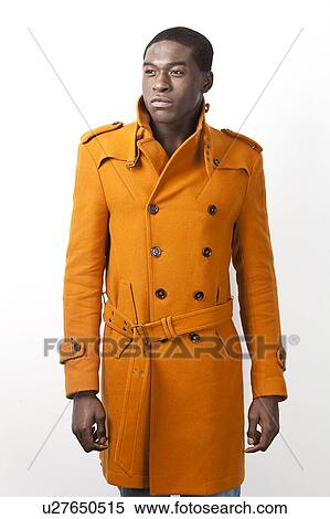 Stock Photography - Young African American man in orange trench coat standing against white background. Fotosearch