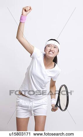 Stock Image - Young Asian female tennis player celebrating her success against white background. Fotosearch