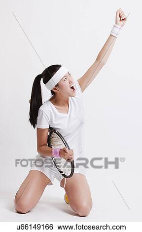 Stock Photograph - Young Asian female tennis player celebrating her success against white background. Fotosearch