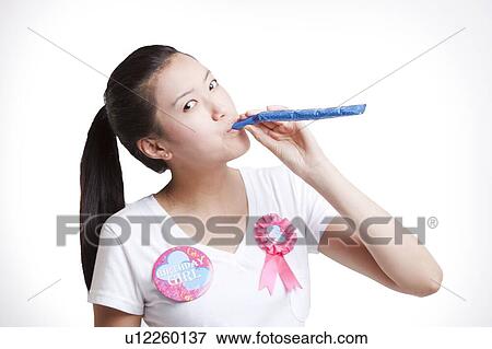 Stock Photo - Young Asian woman blowing noisemaker against white background. Fotosearch