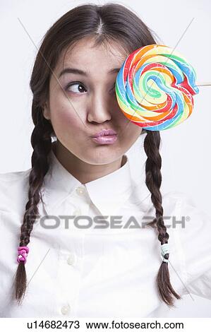 Stock Image - Young Asian woman holding a multicolored lollipop against white background. Fotosearch