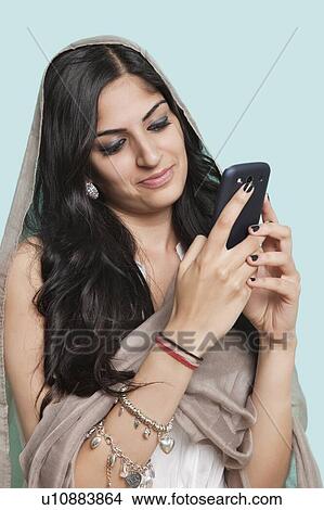 Picture - Young Asian woman in traditional clothing text messaging against blue background. Fotosearch