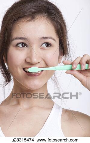 Young Asian woman in white tank top brushing teeth against white background View Large Photo Image Picture - Young Asian woman in white tank top brushing teeth against white background. Fotosearch