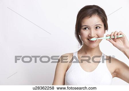 Young Asian woman in white tank top brushing teeth against white background View Large Photo Image Stock Photo - Young Asian woman in white tank top brushing teeth against white background. Fotosearch