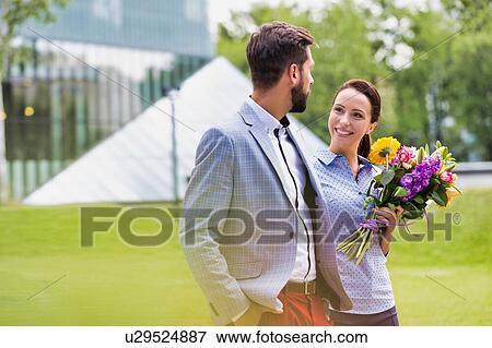 Stock Photo - Young attractive business couple walking in park while the woman is holding boquet of flowers. Fotosearch