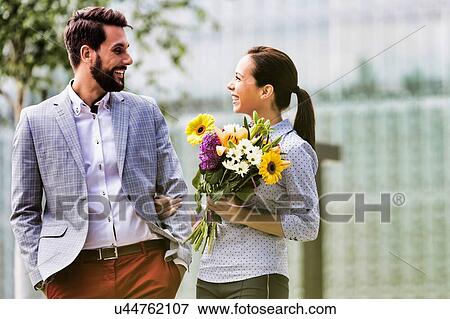 Stock Photo - Young attractive business couple walking in park while the woman is holding boquet of flowers. Fotosearch